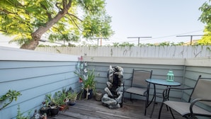 A wooden deck with potted plants, a stone sculpture, and outdoor furniture. - The Madison (Pasadena)