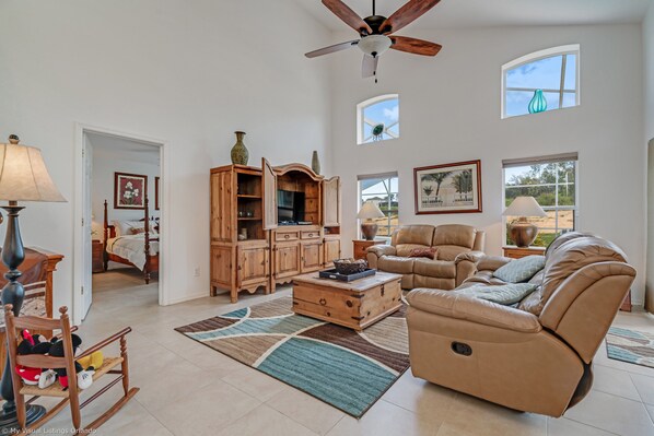A spacious living room with a large leather sofa, wooden cabinet, and a ceiling fan.