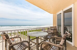 A balcony with a table and chairs, overlooking the ocean. - Oceania Beach Club by Ocean Properties (New Smyrna Beach)