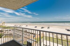 Une vue sur la plage depuis un balcon, avec un parking et un poste de surveillance des sauveteurs en arrière-plan.