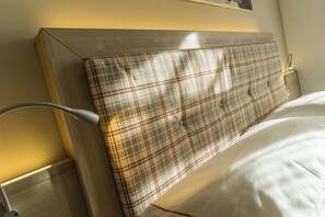 Une tête de lit à motifs écossais, une lampe de chevet et un couvre-lit blanc.