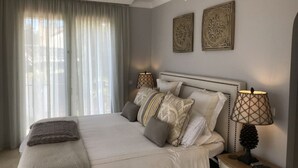 A neatly arranged bedroom with a large bed, two bedside lamps, and two decorative wall pieces. - 5 bedroom villa located in the heart of the golf valley. Perfect for families! (Andalucía)