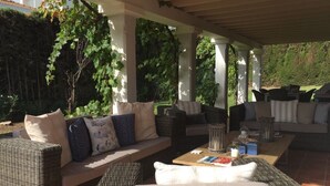 A covered outdoor seating area with wicker furniture, including sofas and a coffee table, under a pergola with columns. - 5 bedroom villa located in the heart of the golf valley. Perfect for families! (Andalucía)