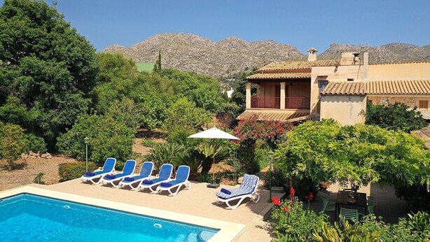 Ein Pool mit Liegestühlen, ein Gebäude mit Balkon und eine Bergkulisse.