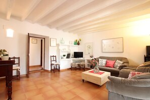 A living room with a wooden dining table, two chairs, a sofa, a coffee table, and a television.