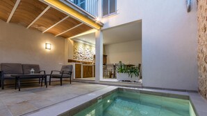 A modern outdoor pool area with a stone wall, seating, and a kitchen visible in the background. - BUGERA. Beautiful restored house in Pollensa (Pollensa)