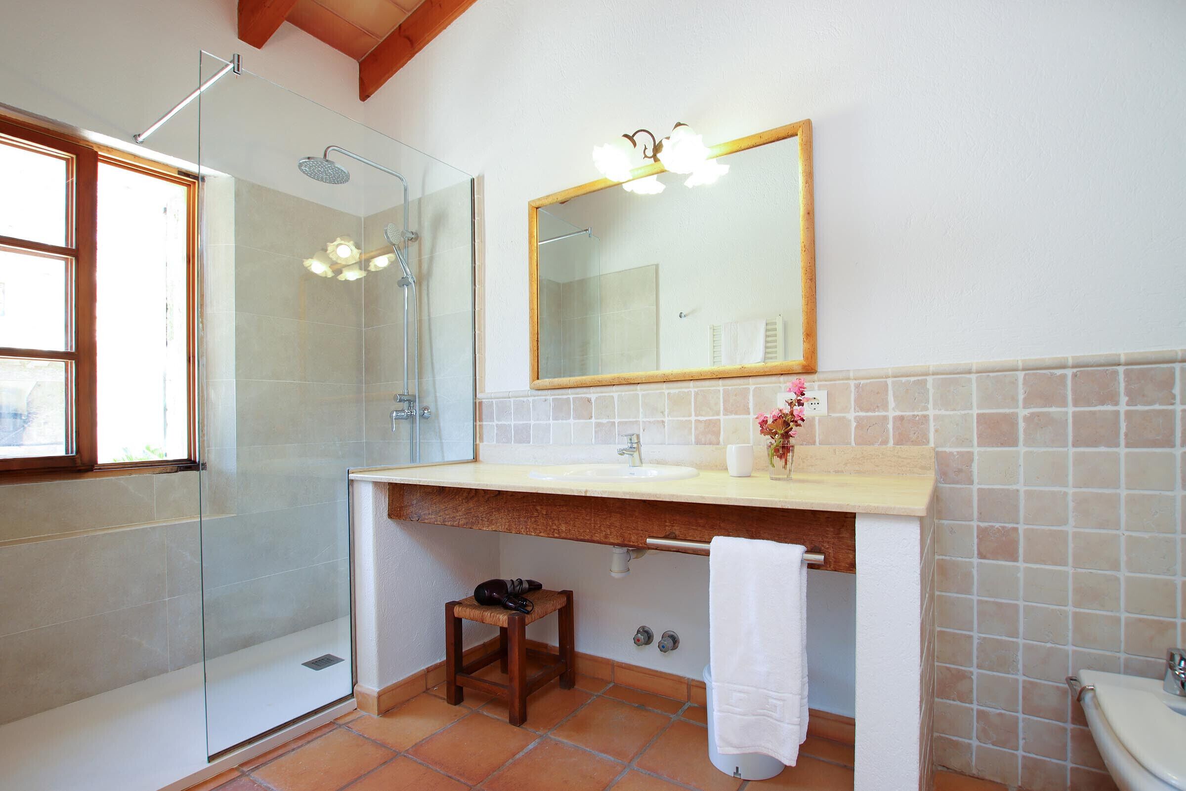Un bagno con cabina doccia in vetro, uno sgabello di legno, un asciugamano bianco e uno specchio sopra il lavandino.