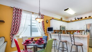 Une cuisine moderne avec des meubles blancs, un coin repas avec des chaises rouges et vertes, et un bar avec des tabourets.