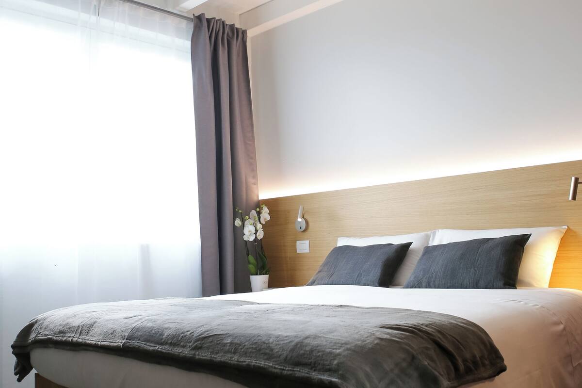 Une chambre d’hôtel moderne avec un lit en bois, une table de chevet avec une lampe et une fenêtre avec des rideaux.