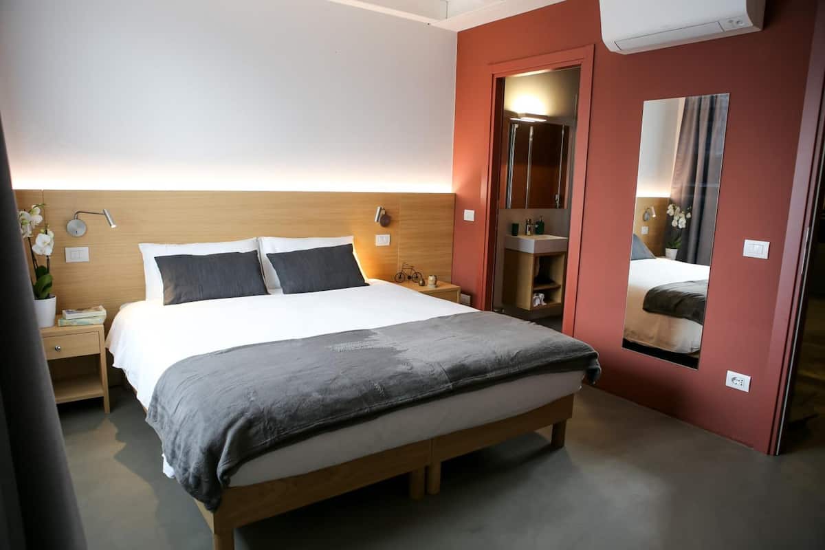Une chambre d’hôtel bien aménagée, avec un grand lit, des tables de chevet, une petite table d’appoint, un miroir et une petite salle de bain.