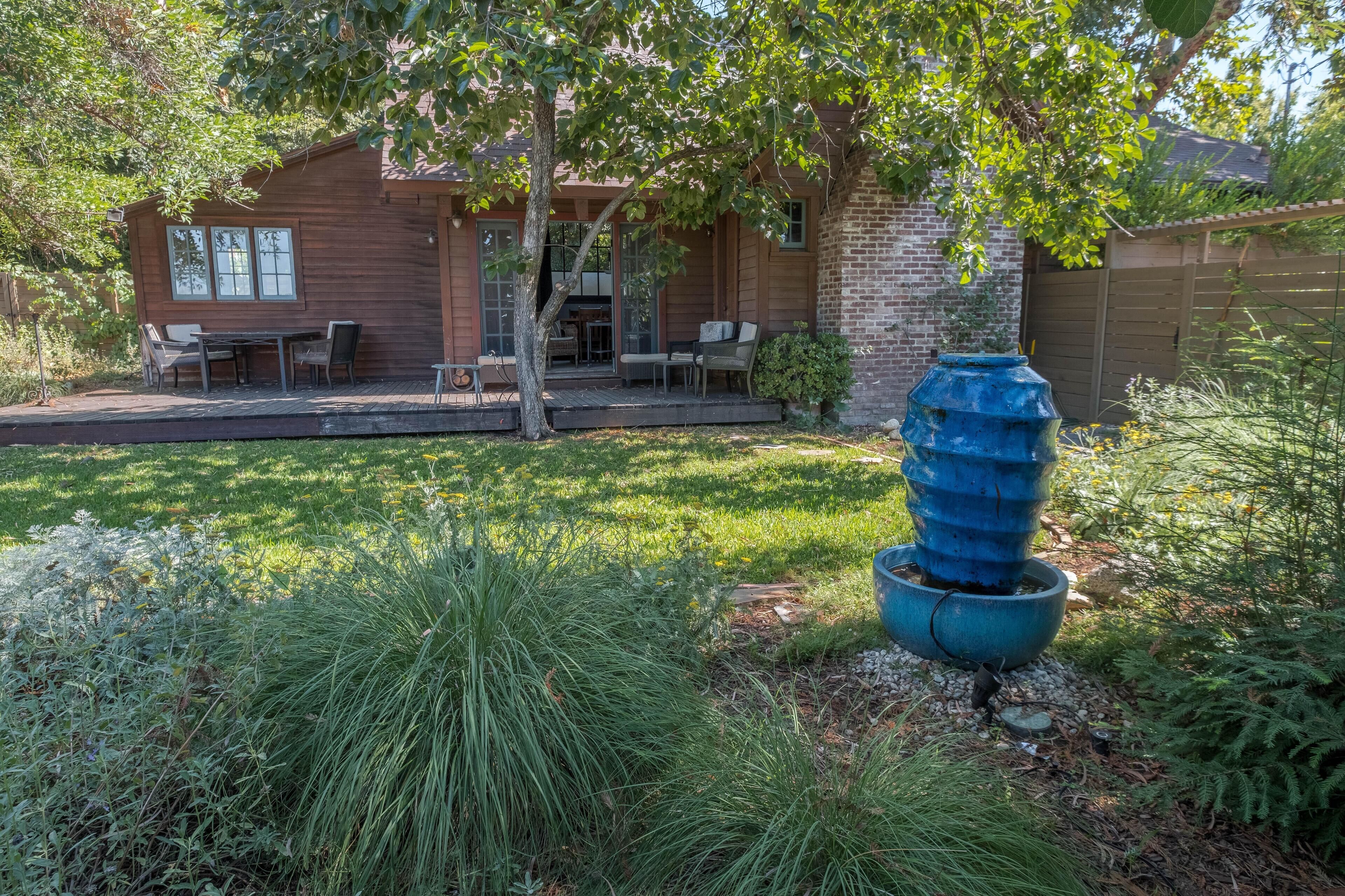 Une maison en bois avec un patio, un espace salon extérieur et un grand bac à fleurs bleu.