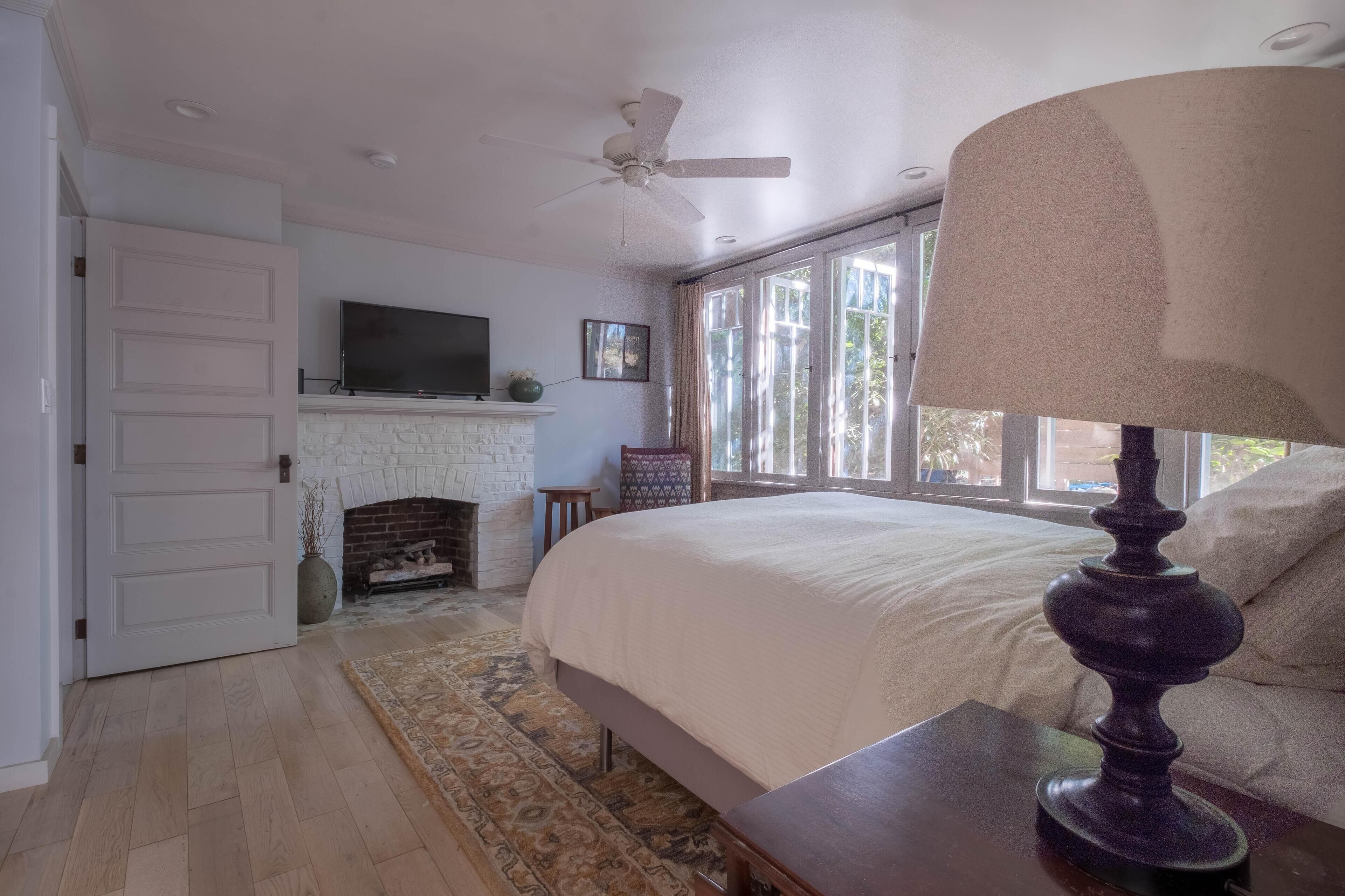 A bedroom with a bed, a television, a fireplace, and a window with curtains.