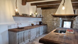 A rustic kitchen with a wooden island, stone walls, and exposed beams. - Casa Giogano (San Leo)
