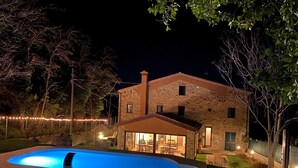 A stone house with a swimming pool, outdoor seating, and string lights. - Casa Giogano (San Leo)