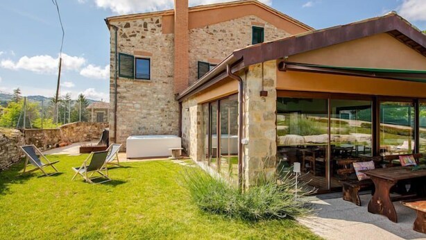 A stone house with a patio, outdoor seating, and a view of the countryside. - Casa Giogano (San Leo)