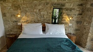 A bed with white linens and a green striped blanket in a room with stone walls and two wooden nightstands. - Casa Giogano (San Leo)