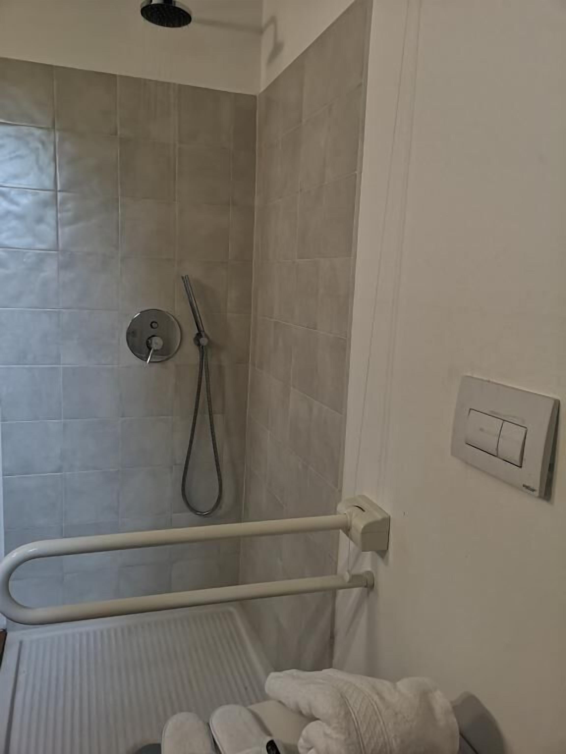 A bathroom with a shower, a handrail, a towel, and a light switch.