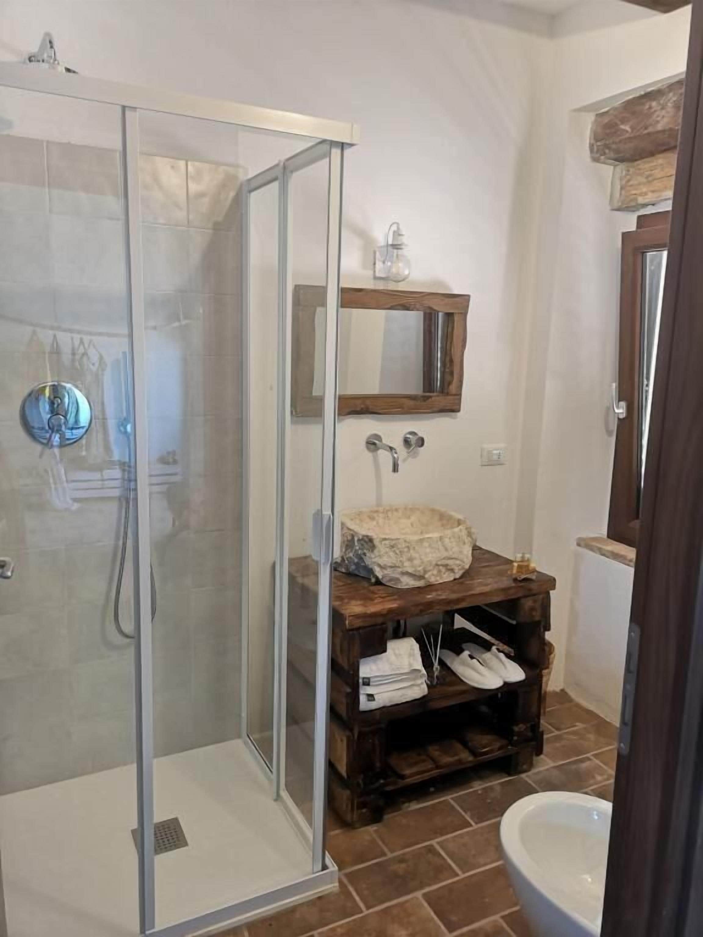 A bathroom with a glass-enclosed shower, a wooden vanity with a sink, and a mirror above it.