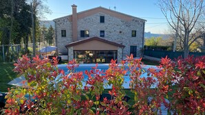 A stone building with a garage, surrounded by a swimming pool and lush greenery. - Casa Giogano (San Leo)