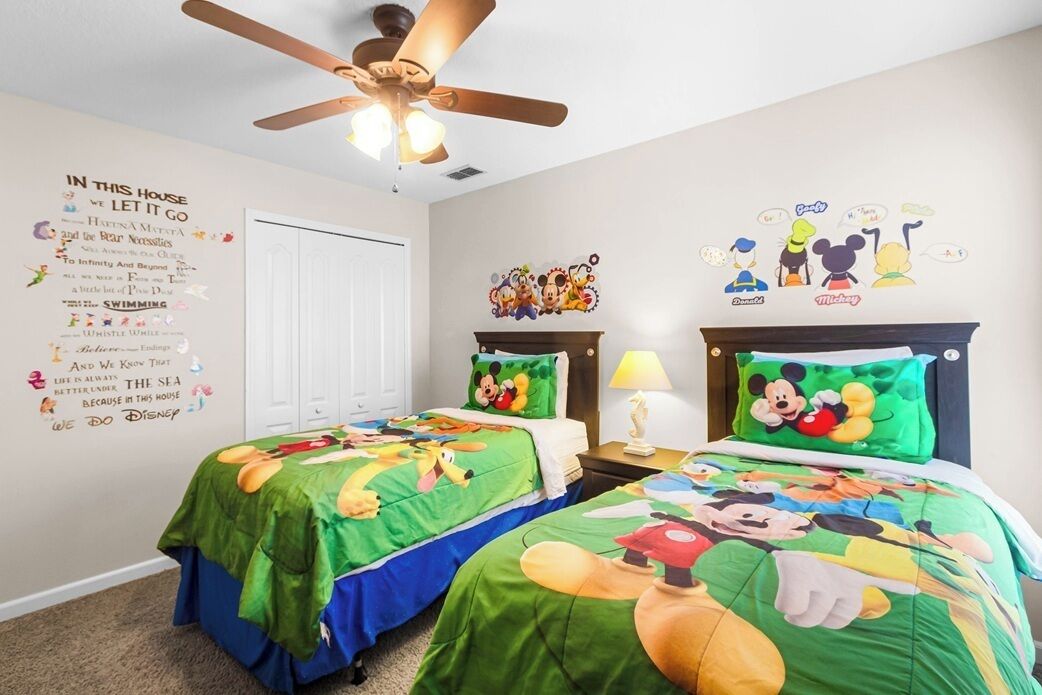 A bedroom with two beds, a ceiling fan, Disney-themed wall decorations, and a motivational quote.
