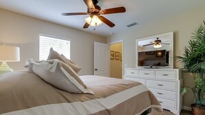 Une chambre à coucher comprenant un lit, un ventilateur de plafond, une commode, un miroir, une lampe et une plante en pot.