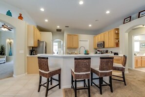 A modern kitchen with a central island, wooden cabinets, and bar stools. - Tennis Courts! Ultimate Backyard Living! Pool with No Rear Neighbors! (Davenport)