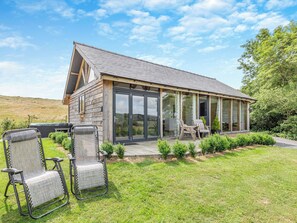 Ein Holzhaus mit überdachter Terrasse, zwei Stühlen und einem Grill.