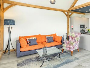 Uma sala de estar com sofá, mesa de centro de vidro, poltrona estampada e luminária.