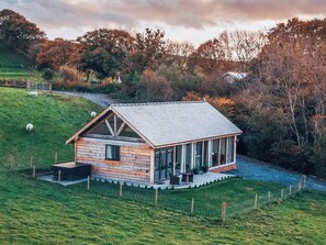 Eine Holzhütte mit geneigtem Dach, einer Veranda mit Sitzgelegenheiten und einem eingezäunten Garten.