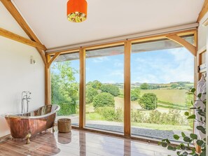 Una habitació àmplia amb un gran finestral, una banyera i una estructura de sostre de fusta.