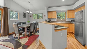 A modern kitchen with wooden cabinets, a stainless steel refrigerator, and a dining area with a table and chairs.