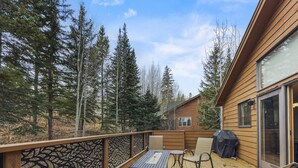 A wooden deck with outdoor furniture, a grill, and a view of a forested area.