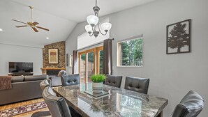 A spacious living room with a large dining table, leather chairs, a fireplace, and a television.