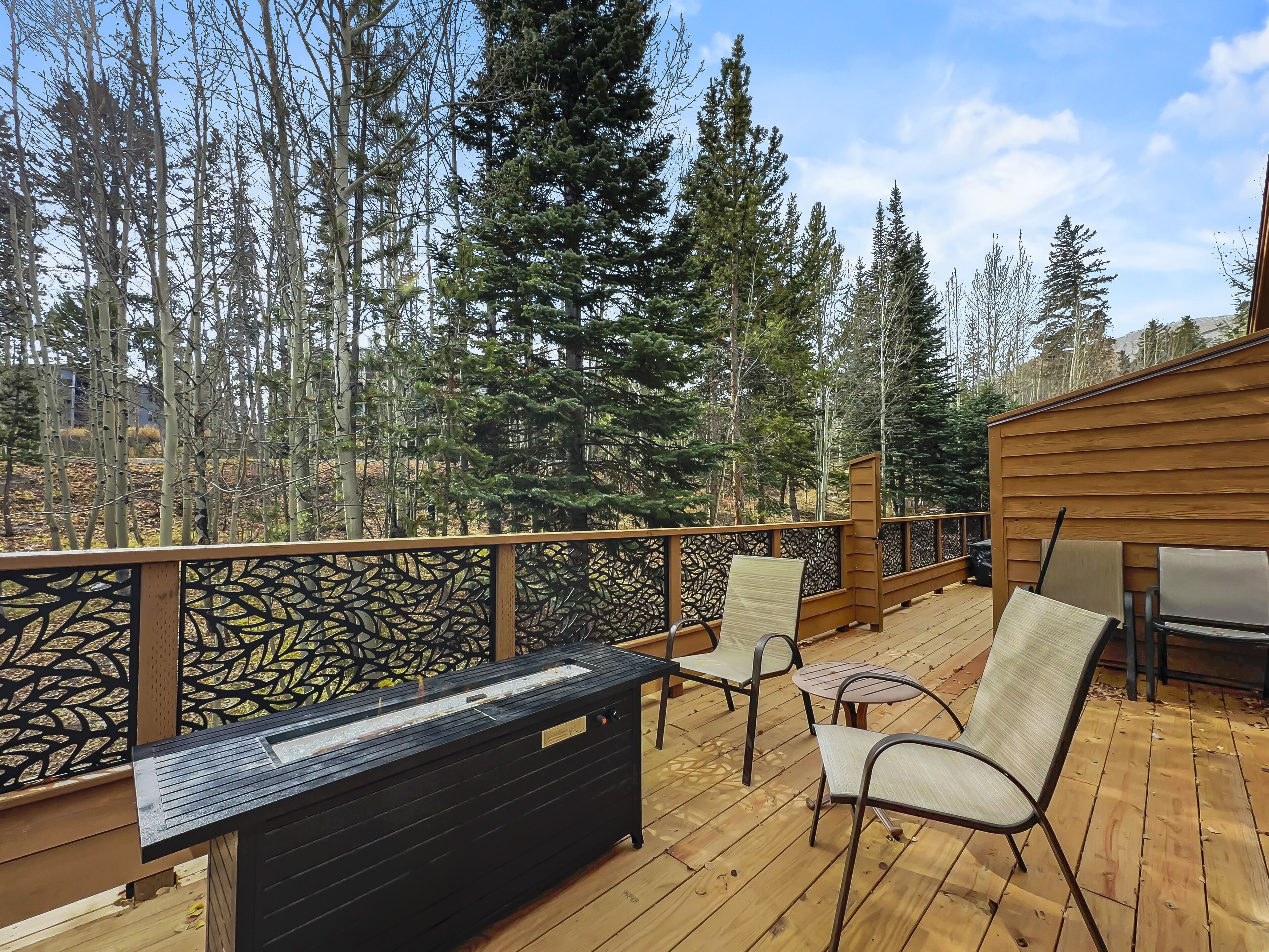 A wooden deck with a black bench, two chairs, and a table.