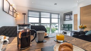 Uma sala de estar moderna com uma janela grande, uma mesa de centro com itens de café da manhã, um sofá e uma TV.