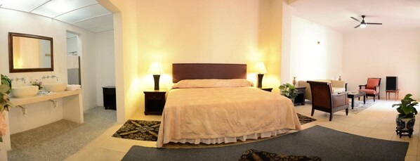 A hotel room with a bed, bedside tables, a desk, a chair, a mirror, and a ceiling fan.