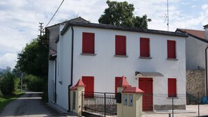 Un immeuble de deux étages avec des volets rouges et une entrée fermée par un portail.