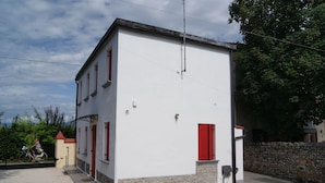 Un bâtiment à deux étages, doté d’une façade blanche, de volets rouges et de fondations en pierre.