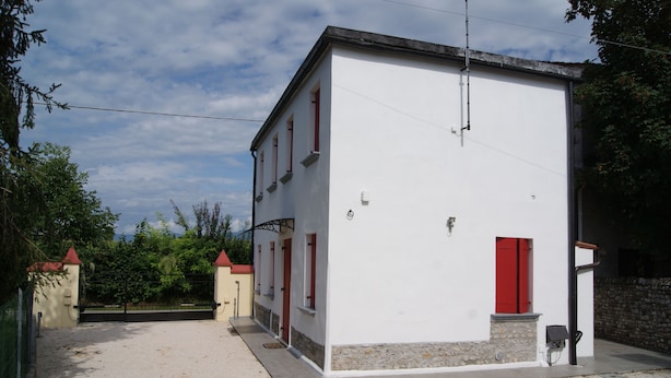 Un bâtiment blanc avec des portes et des fenêtres rouges, une allée gravillonnée et un mur en pierre.