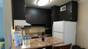 A compact kitchen with dark cabinets, a granite countertop, a sink, and a refrigerator. There are two chairs, a trash bin, and a welcome sign on the counter. - 1st Floor Highlands Hideaway (Spectacular Views) (Birmingham)