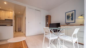 Een moderne keuken met witte kasten, een eethoek met een glazen tafel en witte stoelen, en een schilderij aan de muur.