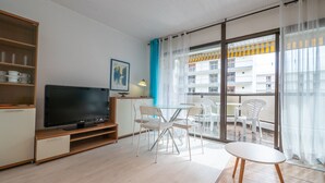 Een moderne woonkamer met een flatscreen televisie, witte meubels, een glazen tafel en een balkon met uitzicht op een gebouw.