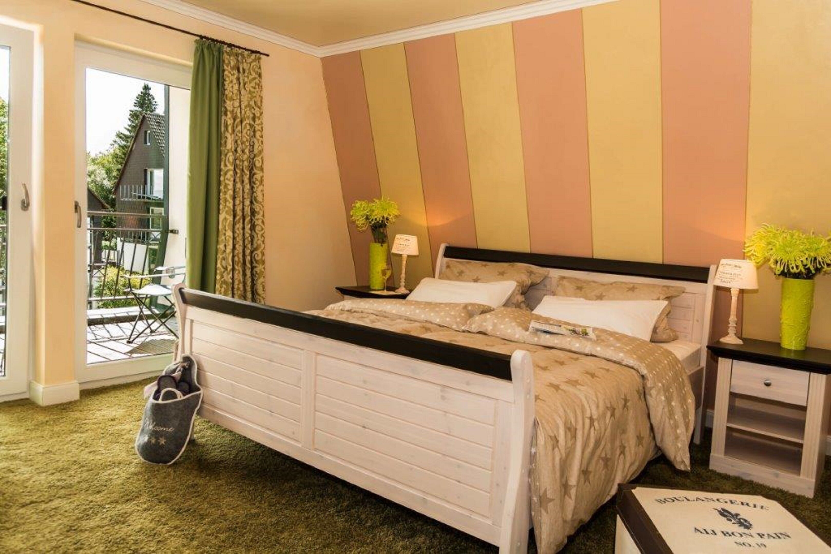 A bedroom with a bed, two bedside tables, a nightstand, a green bag, and a window with curtains.