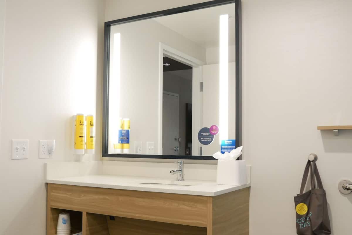 A modern bathroom with a wooden vanity, a large mirror, and toiletries on the counter.