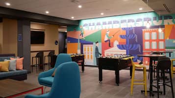 A modern indoor space with a foosball table, comfortable seating, and a colorful mural on the wall.