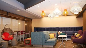 A modern lounge area with a blue sofa, red and purple chairs, a hanging chair, and a dining area with red chairs and tables. - Tru By Hilton Chambersburg, PA (Chambersburg)