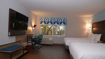 Moderni hotellihuone, jossa on sänky, työpöytä, tuoli, televisio ja ikkuna, josta avautuu näkymä puistoon.