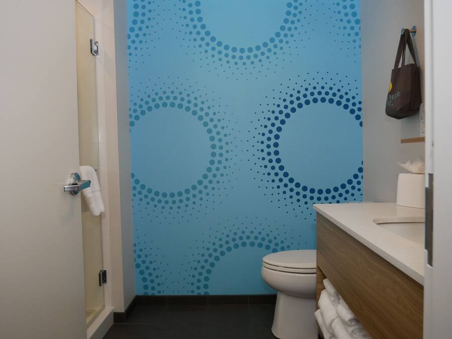 A bathroom with a blue wall featuring a dotted pattern, a white toilet, and a wooden vanity with a towel rack.