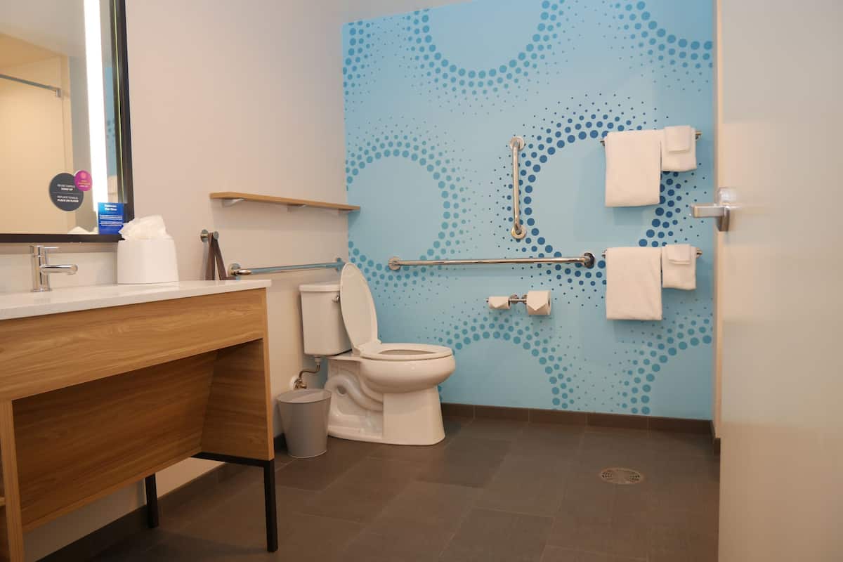 A modern bathroom with a toilet, sink, and handrails.