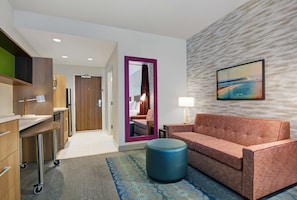 Une chambre d’hôtel moderne avec un canapé, un pouf et un miroir doté d’un cadre violet.